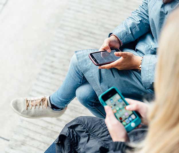 Two students sitting on some steps looking at their iPhones