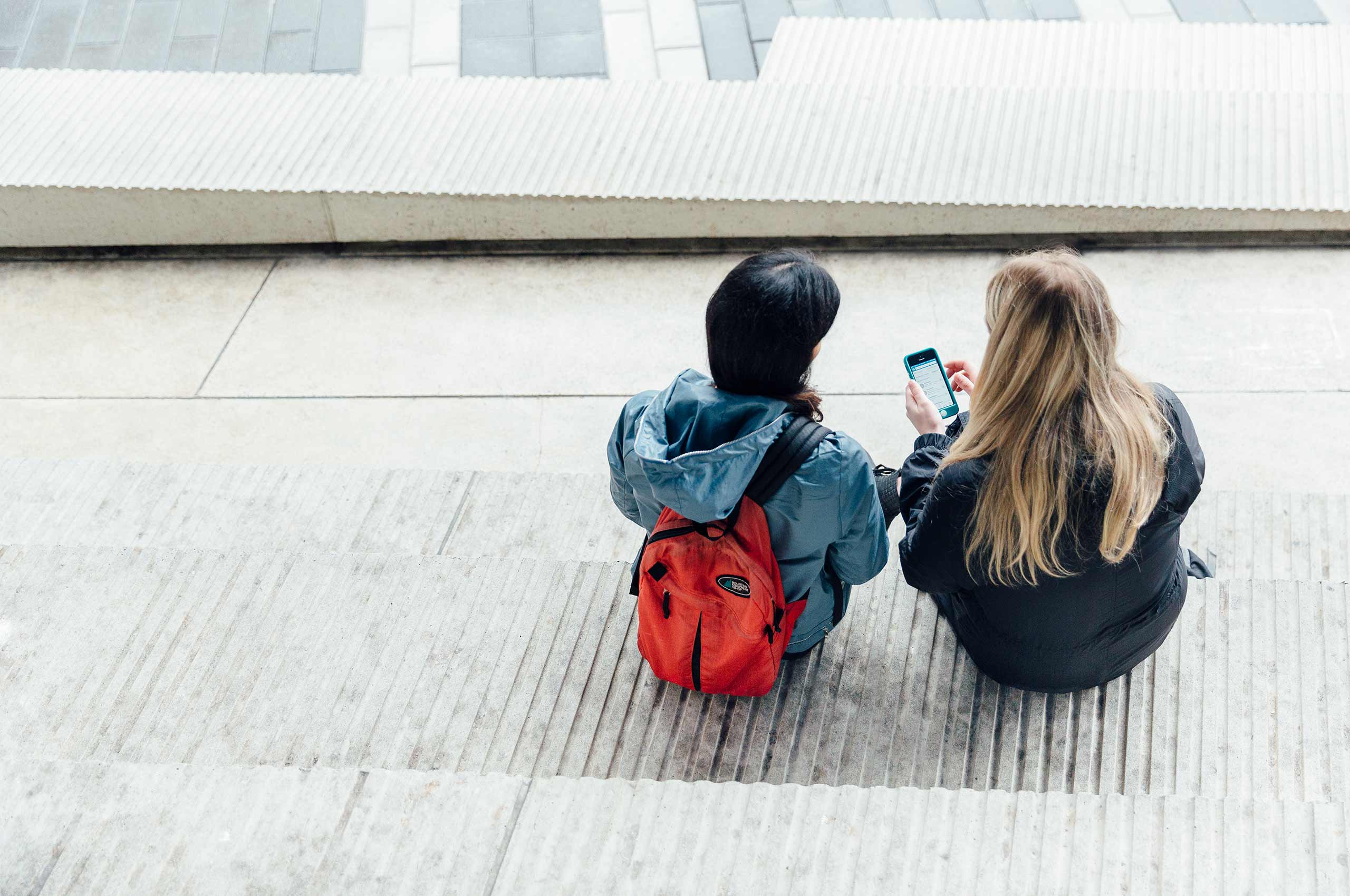 Two students sitting on some steps looking at an iPhone