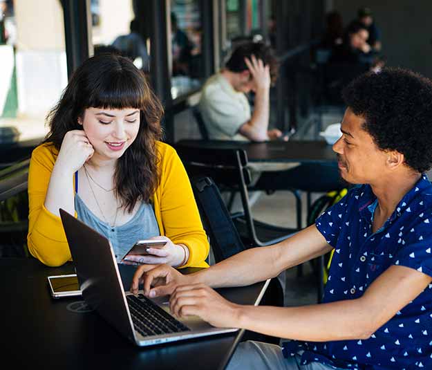 Two students sitting at a cafe on their devices