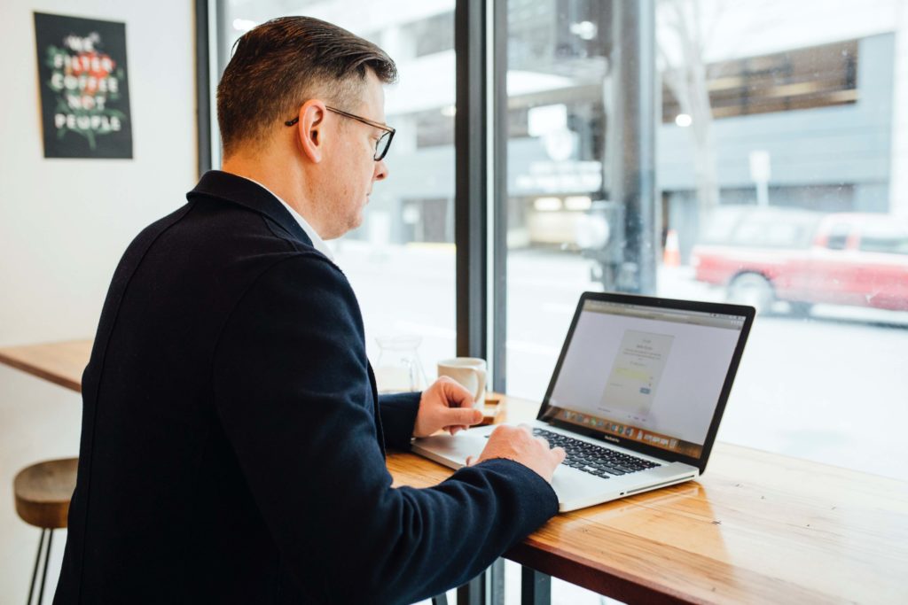 A man wearing a blazer sits in front of an open laptop.