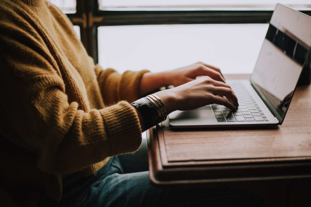 A person wearing a mustard-colored sweater sits in front of an open laptop.