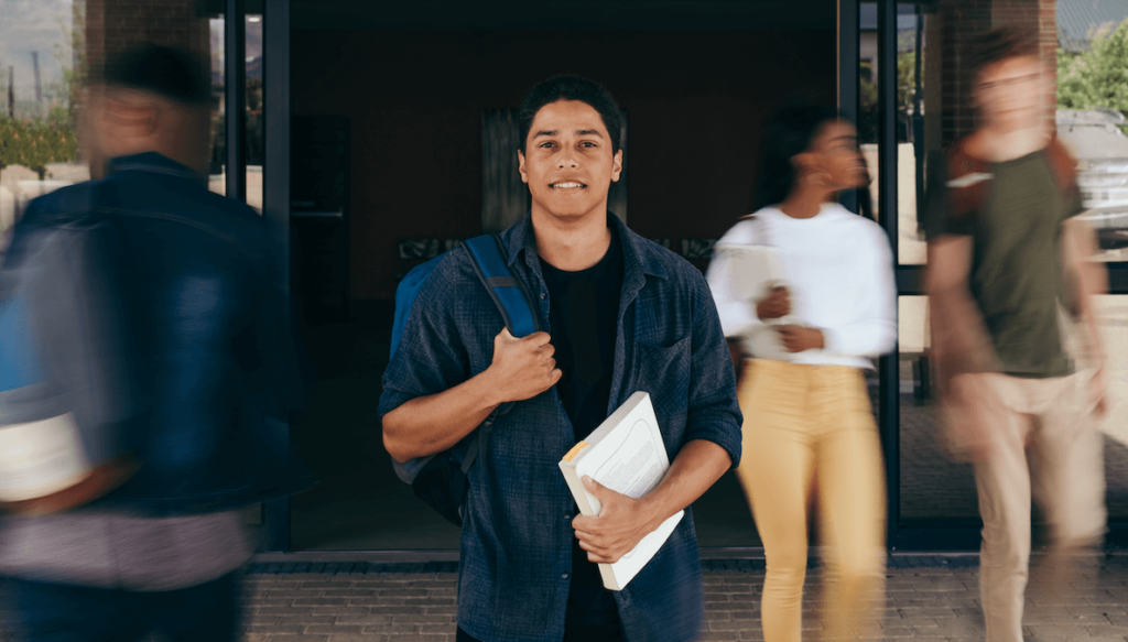 student smiling and walking to class with a textbook in his hand